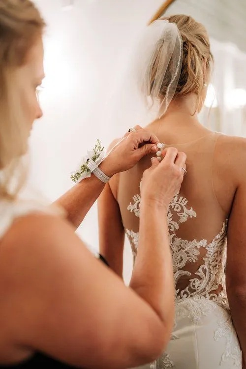 A woman is helping another person put on her dress.