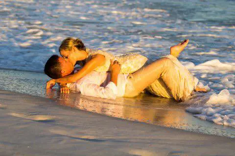 A man and woman kissing on the beach.